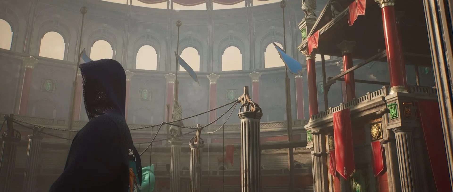 A hooded figure in an ancient arena hung with red banners and lanterns, in cinemascope