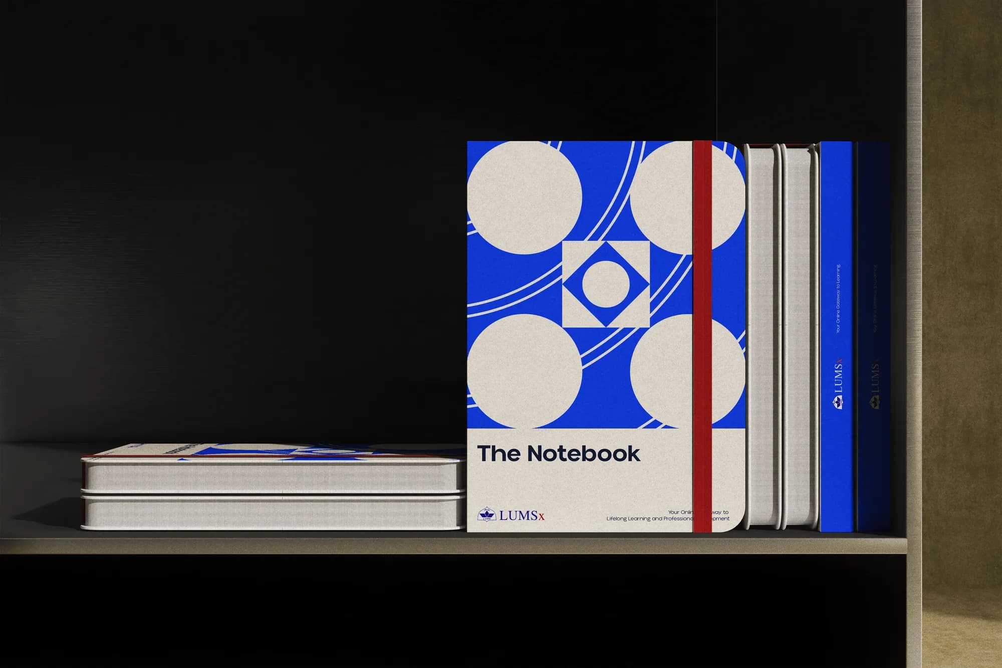 LUMSx notebooks on a shelf, the cover printed with a large blue pattern of circles and shapes