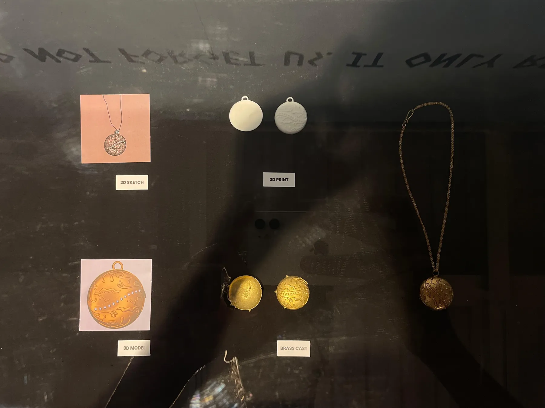 A vitrine tracing the locket from 2D sketch and 3D model to 3D prints, the brass cast halves and the finished locket on its chain
